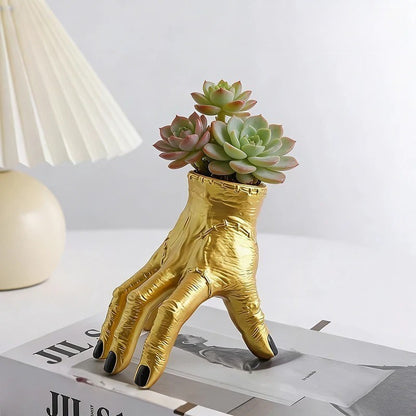 Gold hand-shaped planter with succulents on a magazine