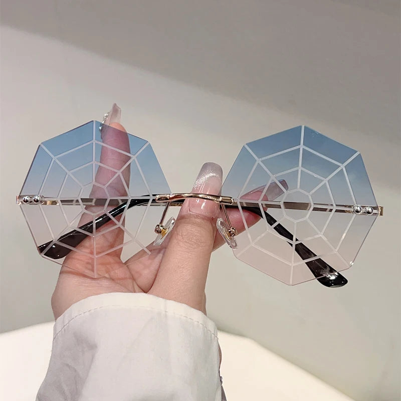 Hand holding a pair of geometric sunglasses with a spider web design against a plain background