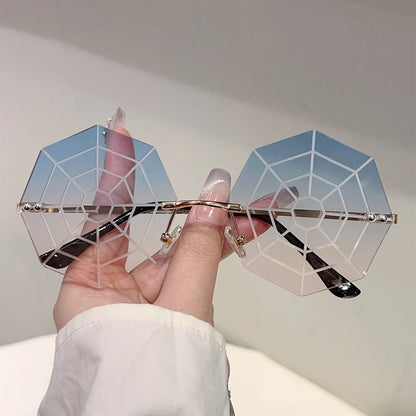 Hand holding a pair of geometric sunglasses with a spider web design against a plain background