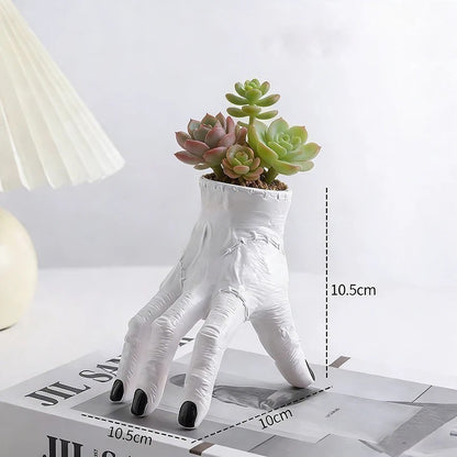 White hand-shaped planter with succulents on a magazine, measurements indicated.