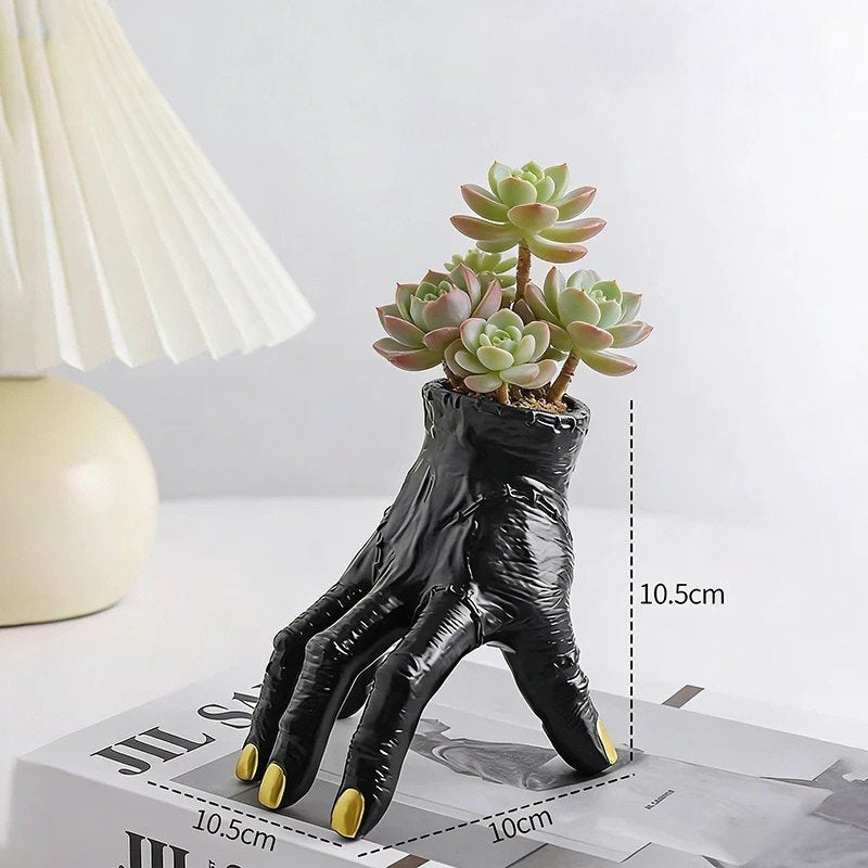 Black hand-shaped planter with succulents on a white surface with measurement details.